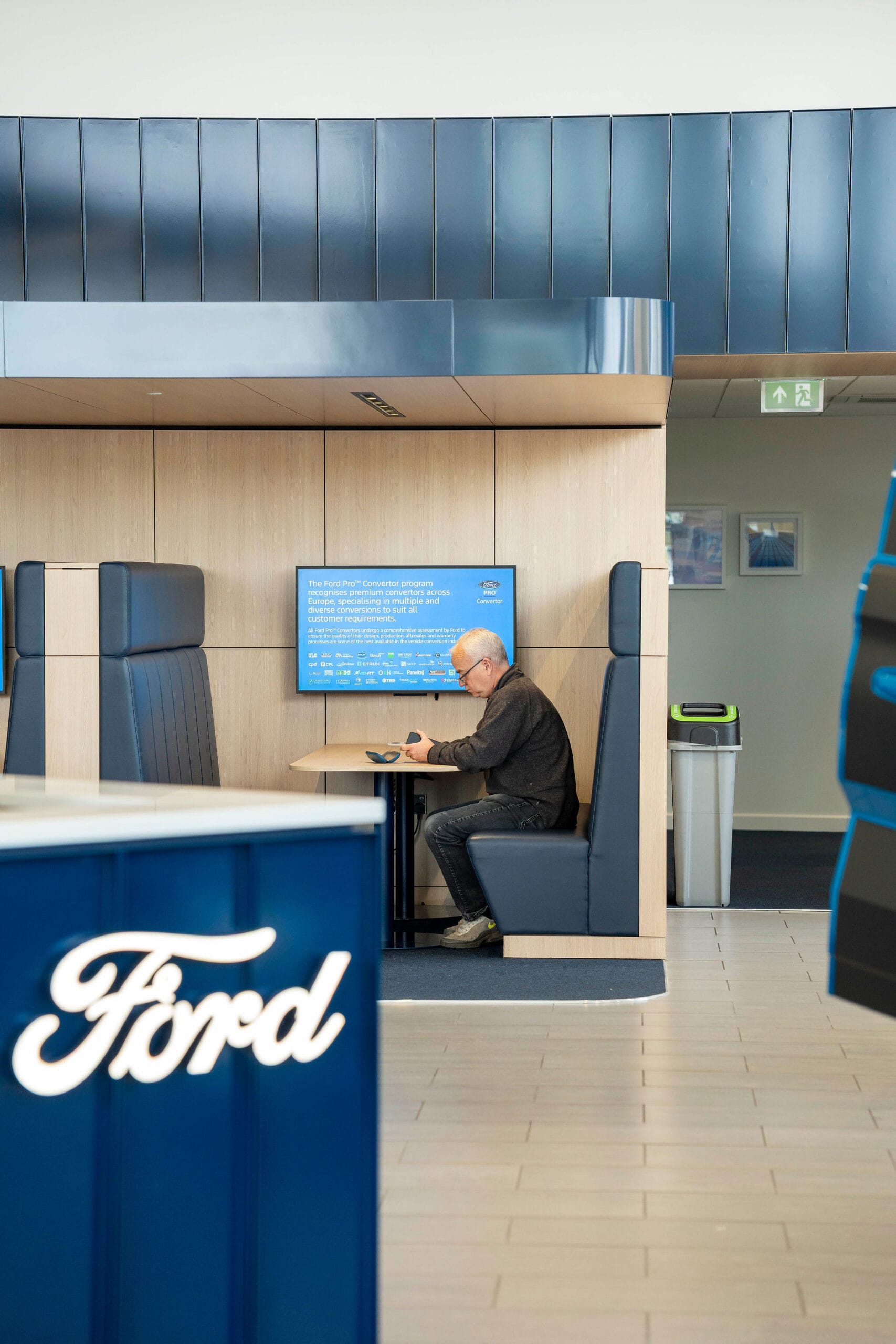 Man sitting in Ford showroom booth using phone